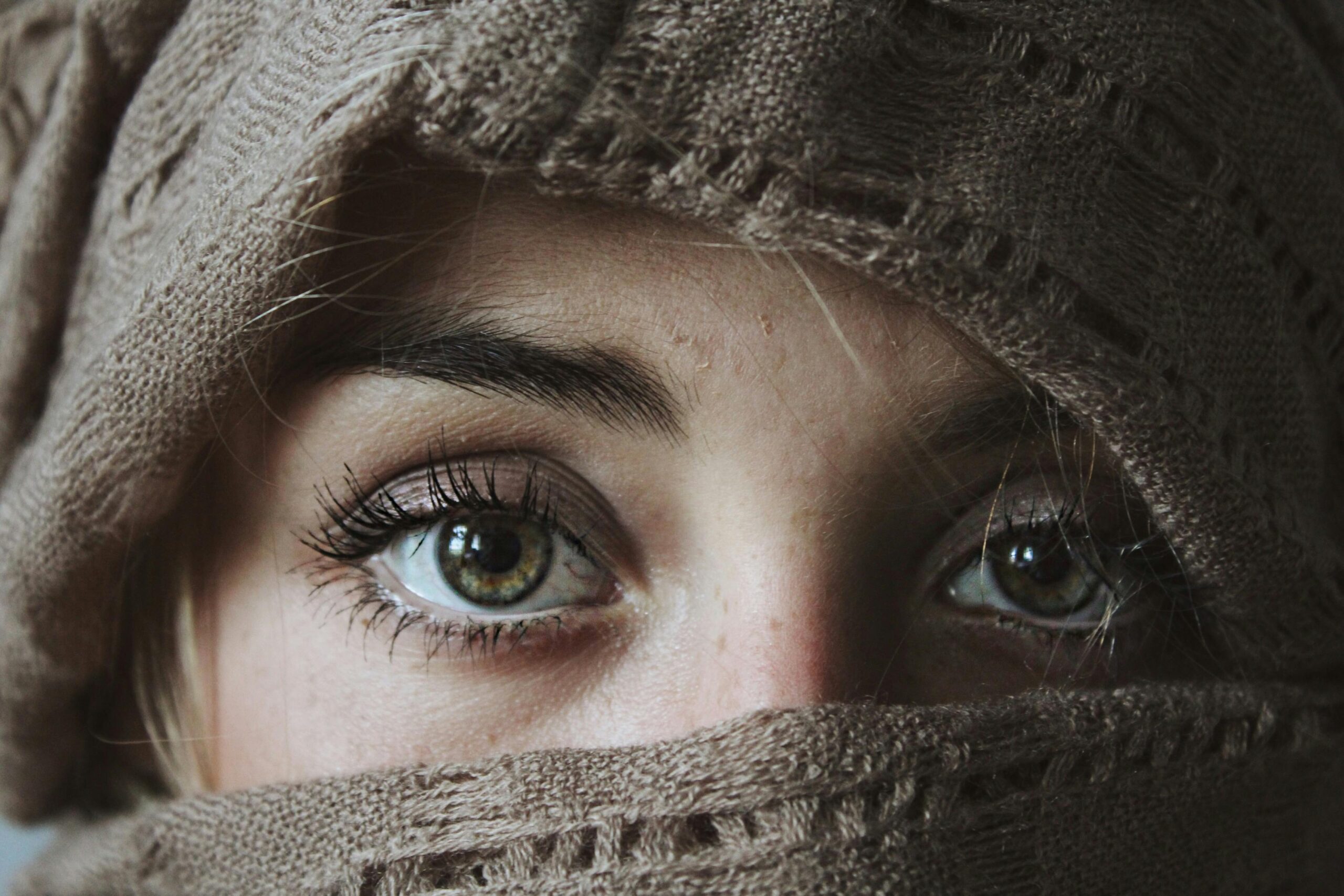 Intense eyes of a woman wrapped in a knitted scarf, showcasing winter fashion.